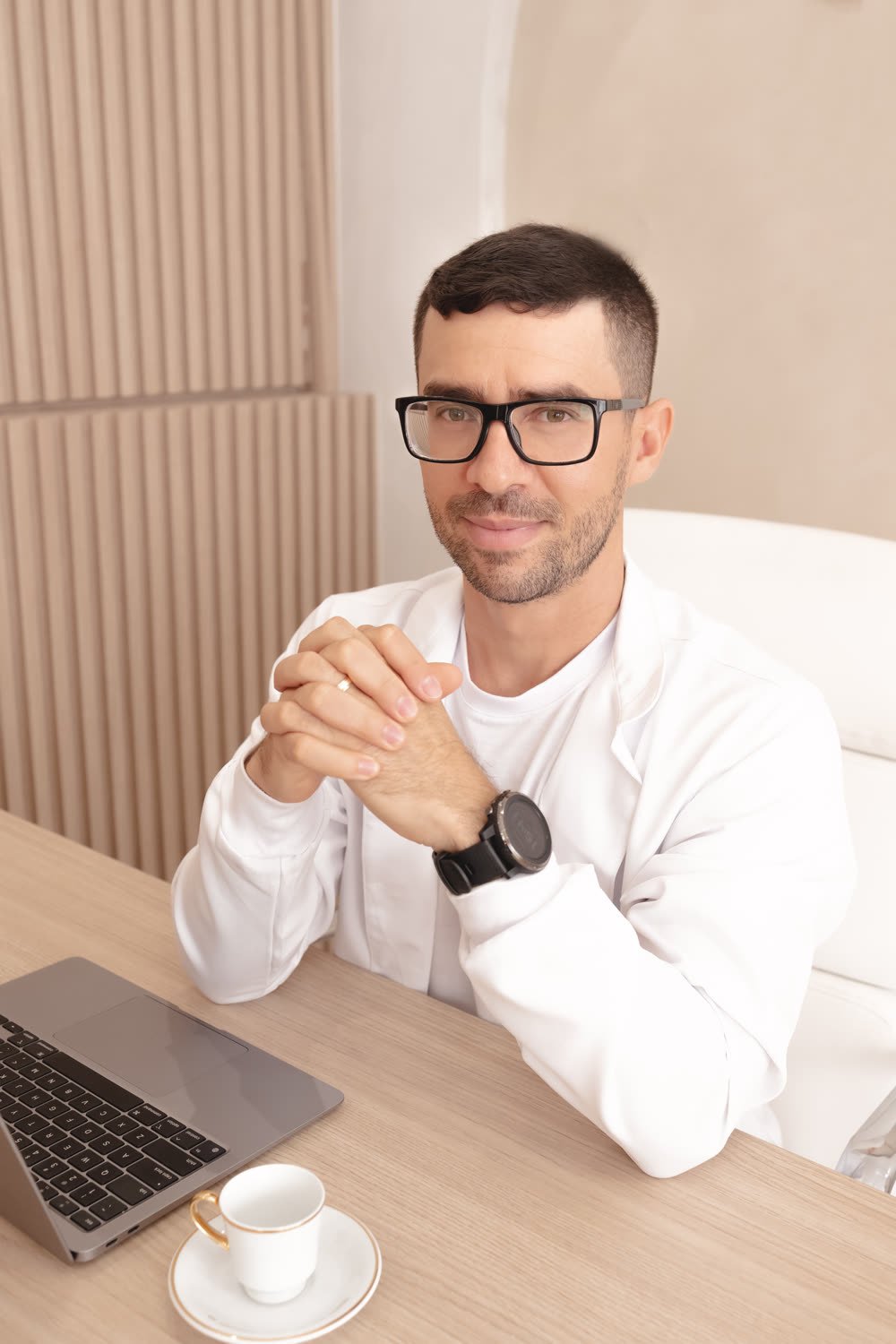 Bruno de Freitas, podólogo da Podoingá Podologia em Maringá, de jaleco branco na mesa do consultório